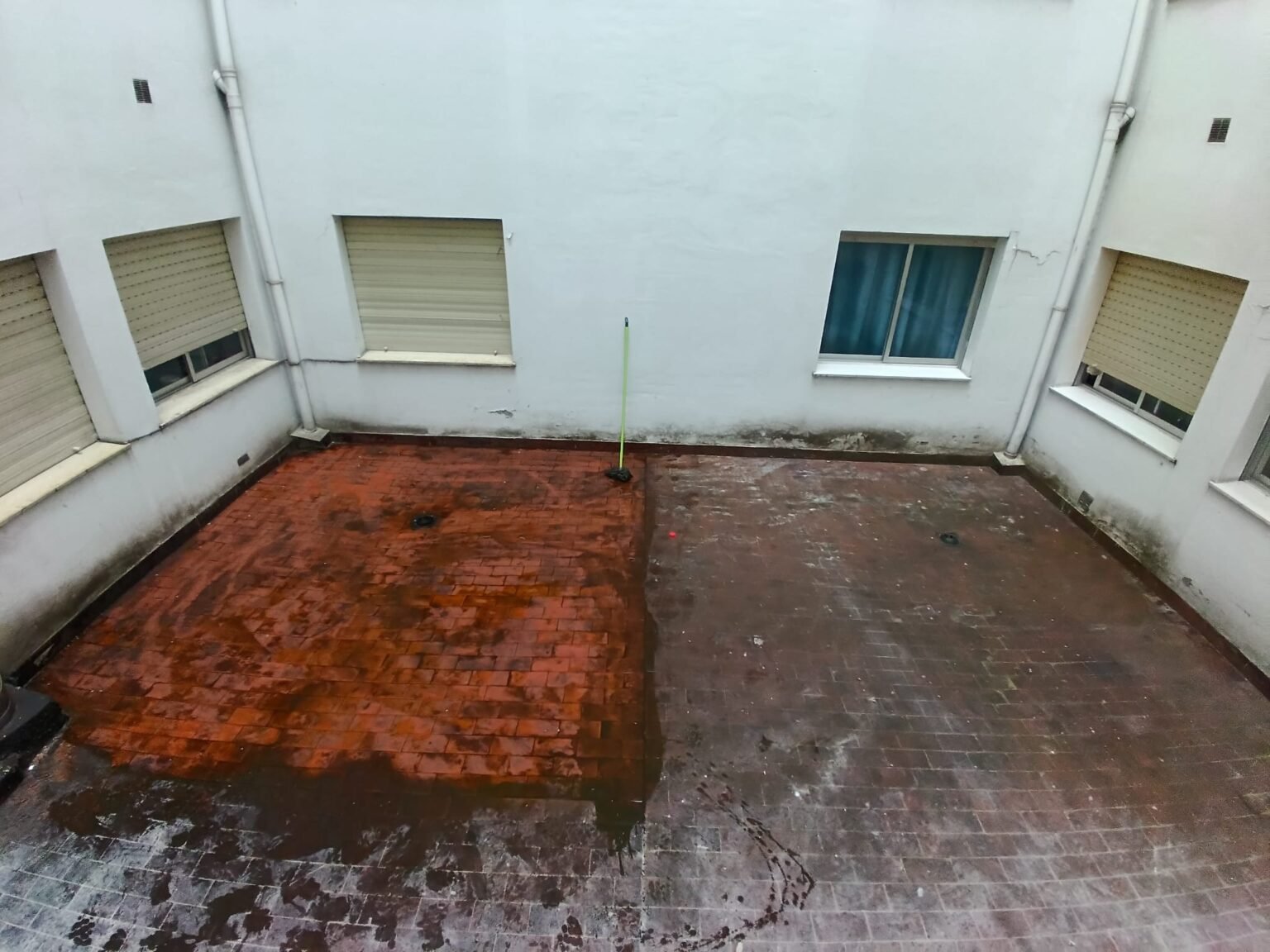 Patio antes de impermeabilizar, con una mancha grande de óxido sobre el suelo de ladrillo