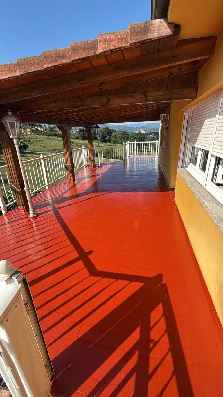 Terraza bajo un porche de madera, con el suelo acabado en rojo y el valle al fondo